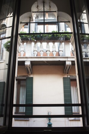 A view through a window of a building with a balcony, green shutters, and a water spigot. - Hotel Corte di Gabriela (Venice)