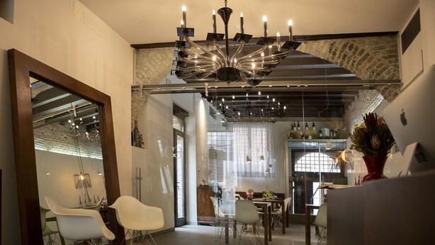 A modern dining area with a chandelier, white chairs, and a glass partition. - Hotel Corte di Gabriela (Venice)