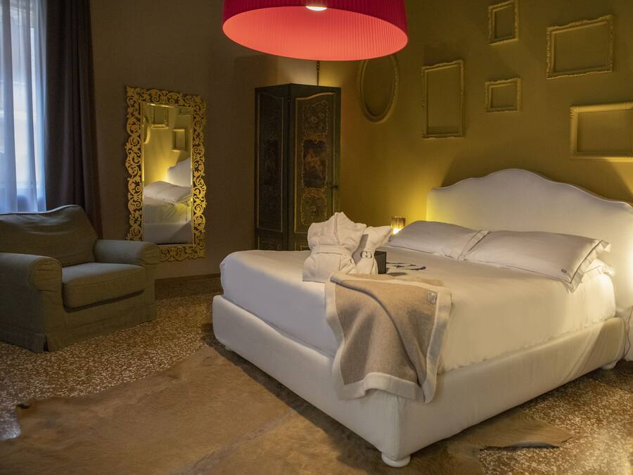 A neatly arranged bedroom with a large bed, a chair, a wardrobe, and a bedside table with a lamp.