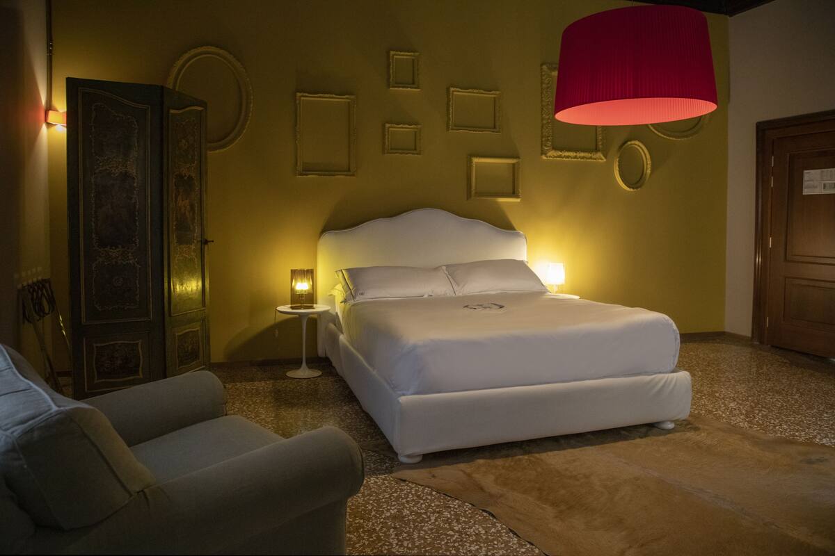 Una camera da letto con un letto, un comodino, una sedia e una lampada rossa.