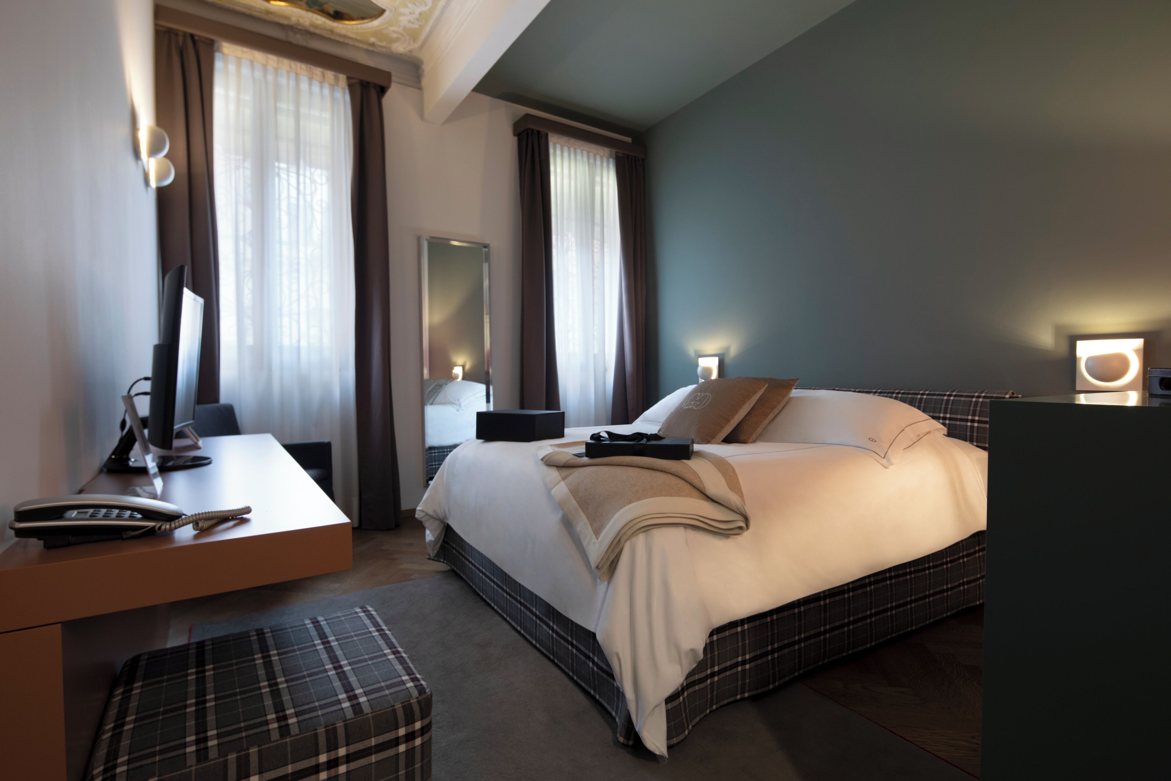Quarto de hotel com cama, mesa de cabeceira, escrivaninha, cadeira e um espelho grande.