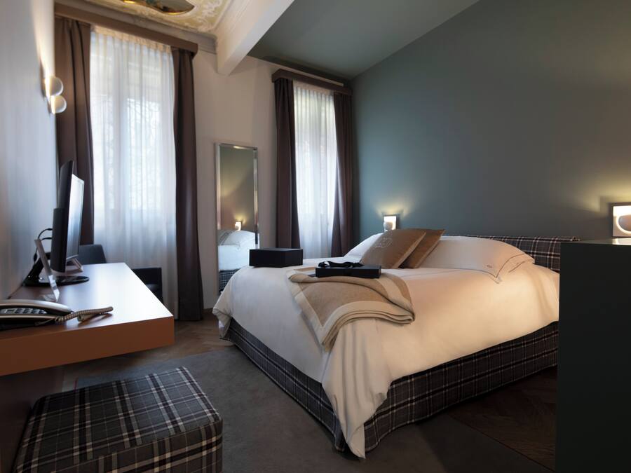 Quarto de hotel com cama, mesa de cabeceira, escrivaninha, cadeira e um espelho grande.