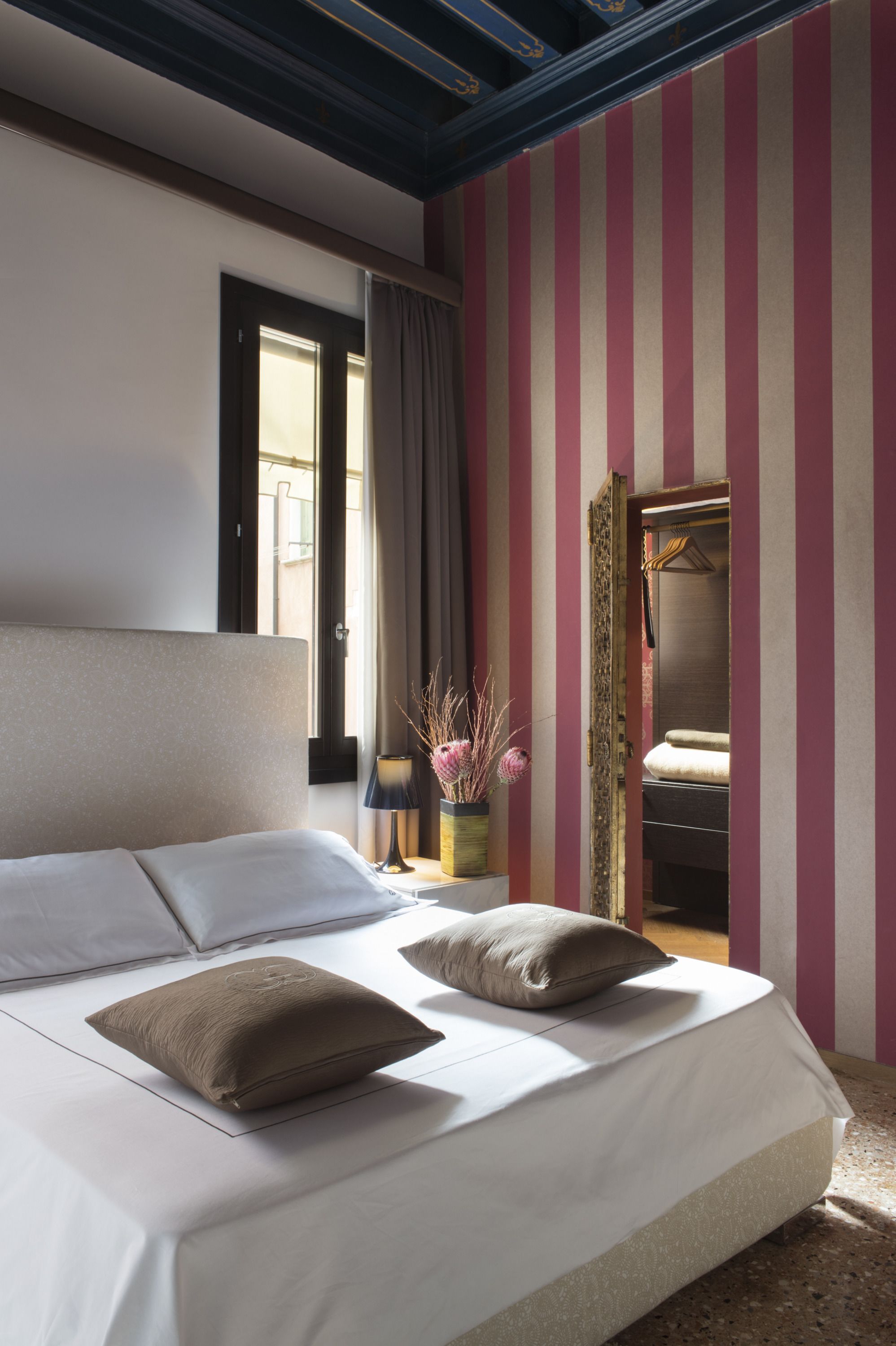 Un dormitorio con una cama grande, una mesita de noche, una lámpara y una ventana con cortinas.