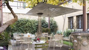 An outdoor patio with a table and chairs, surrounded by greenery and a stone wall. - Hotel Corte di Gabriela (Venice)