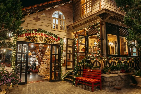 A warmly decorated building with a 'Merry Christmas' sign, wooden architecture, and a bench outside.