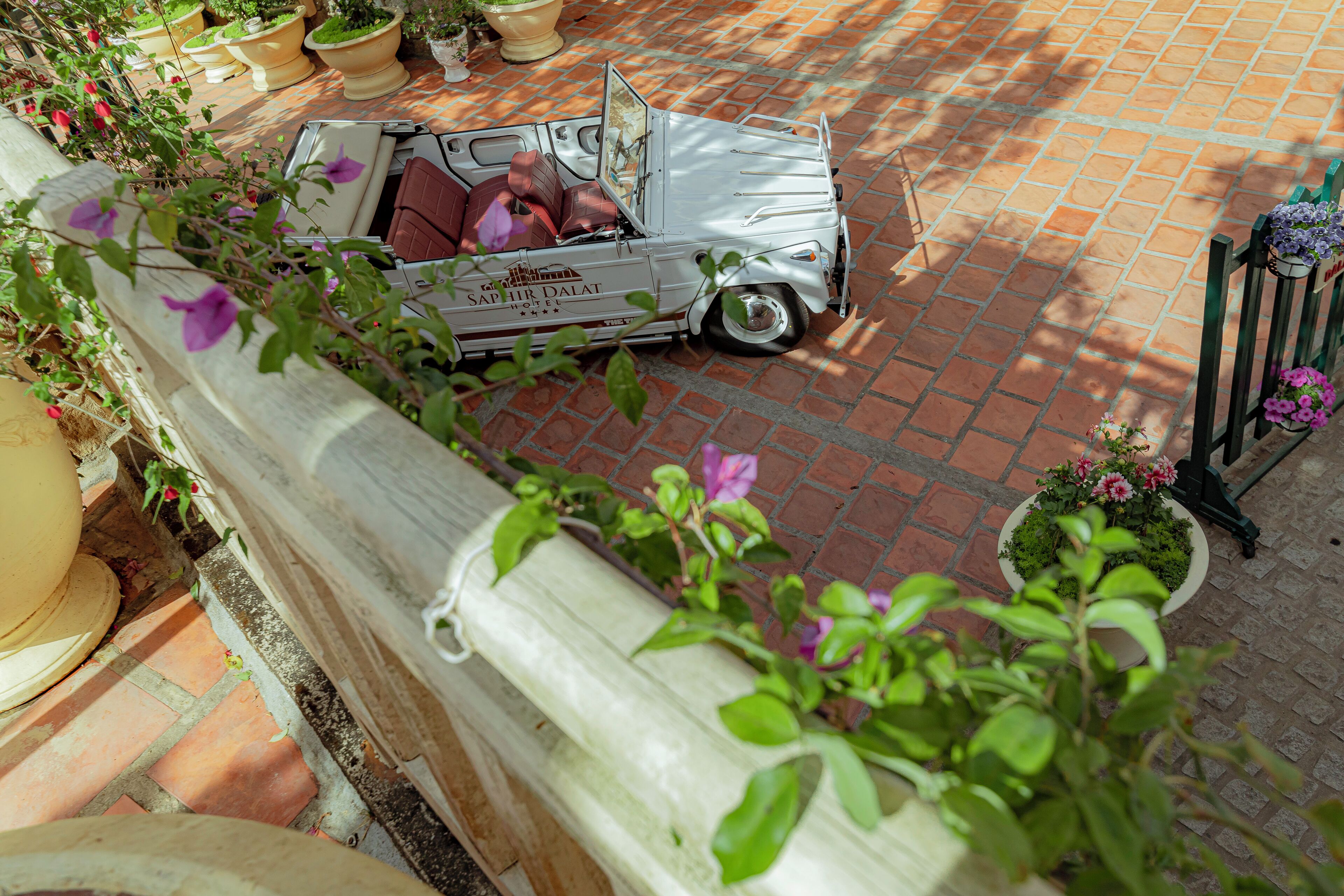 Un coche antiguo estacionado en un camino de ladrillo con plantas en macetas y una valla de madera.