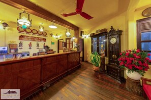 A reception area with a wooden reception desk, multiple clocks, a ceiling fan, and a large clock on the wall. - Saphir Dalat Hotel (Da Lat)