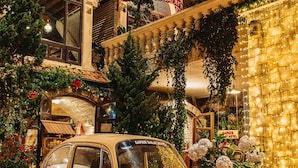 Une voiture ancienne est garée devant un hôtel au style architectural classique, qui se distingue par une grande fenêtre en arc et une façade en briques.