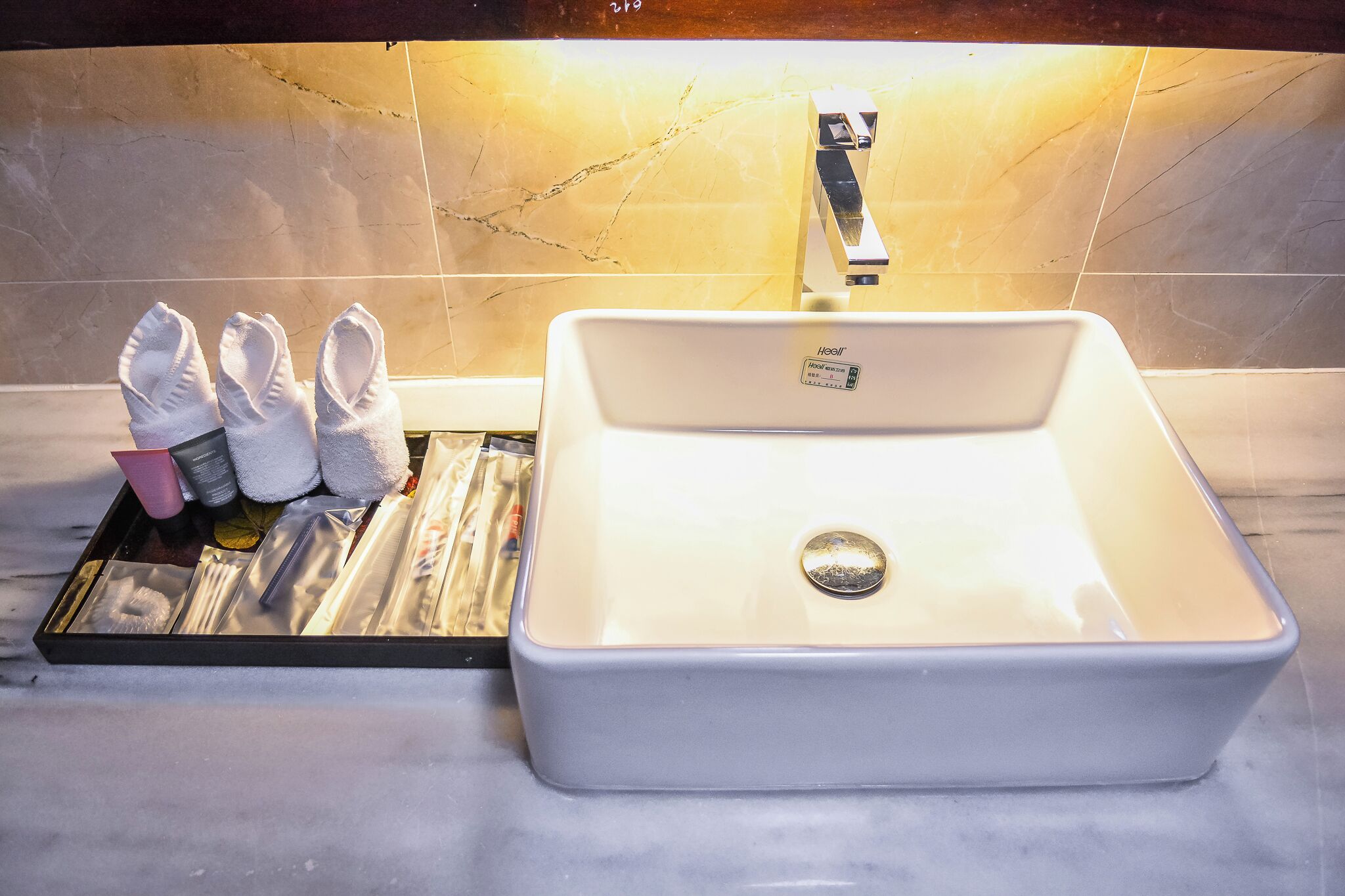 A bathroom with a white sink, a towel rack with towels, and a tray with toiletries.