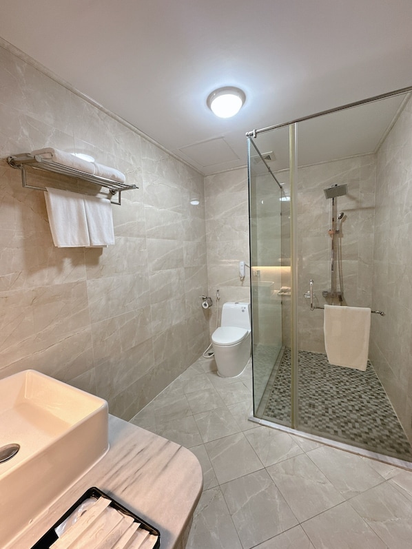 Un baño moderno con cabina de ducha de vidrio, inodoro y lavabo con toallero.