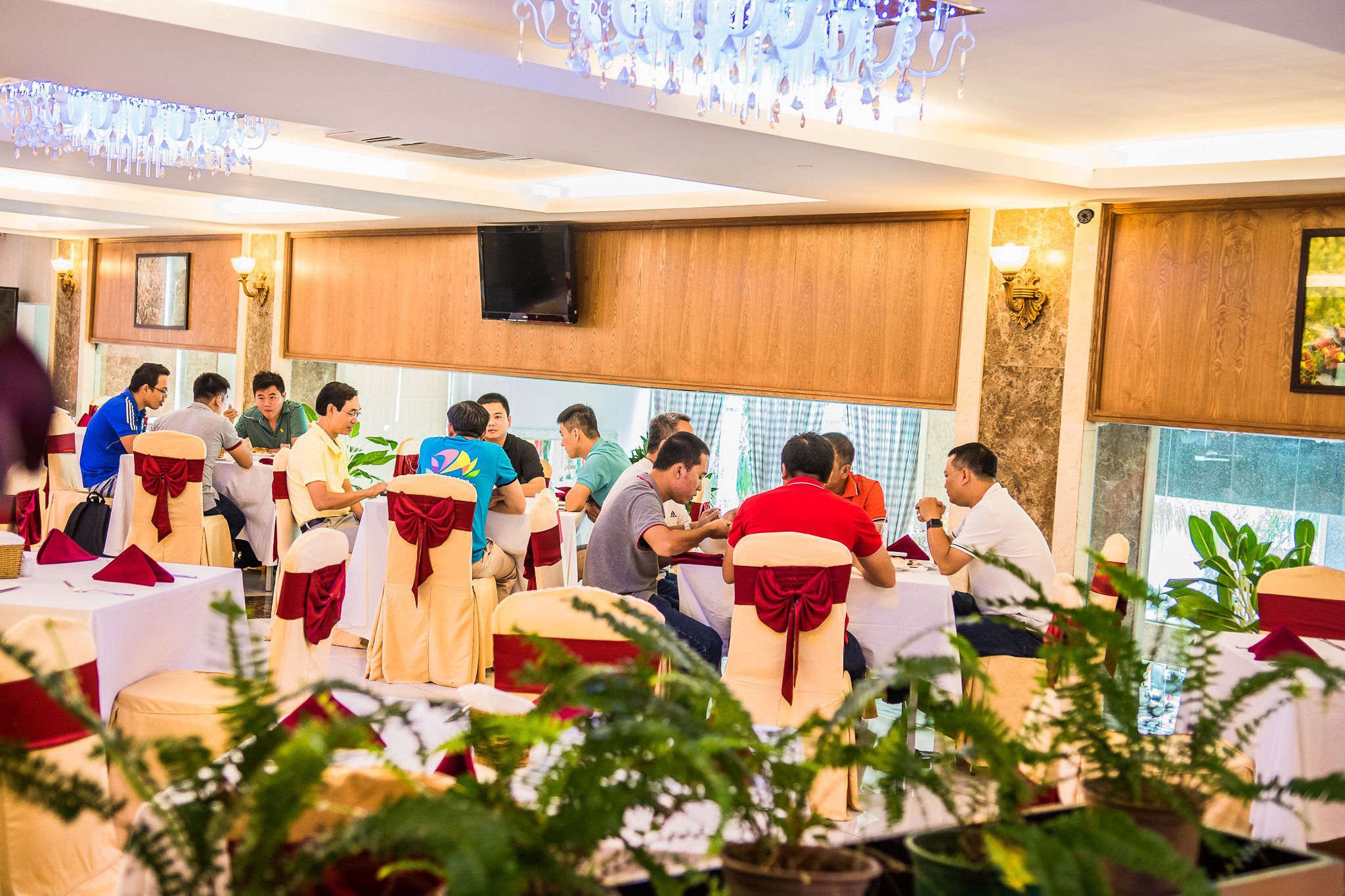 A banquet hall with round tables, guests seated, and a chandelier.
