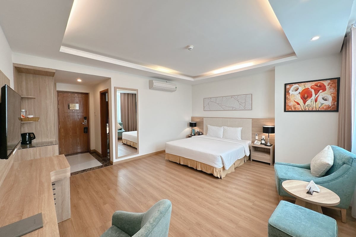 A modern hotel room with a large bed, a desk, a chair, and a small table.