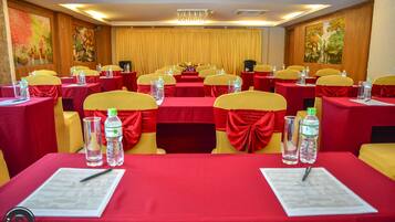 A conference room with rows of tables, each with a red tablecloth, yellow chairs, and water bottles.