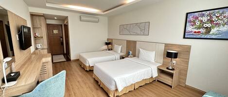 A hotel room with two beds, a desk with a chair, a TV, a bedside table with a lamp, and a painting on the wall.