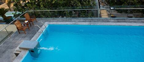 Une piscine avec une terrasse carrelée, des chaises en bois et une petite table.