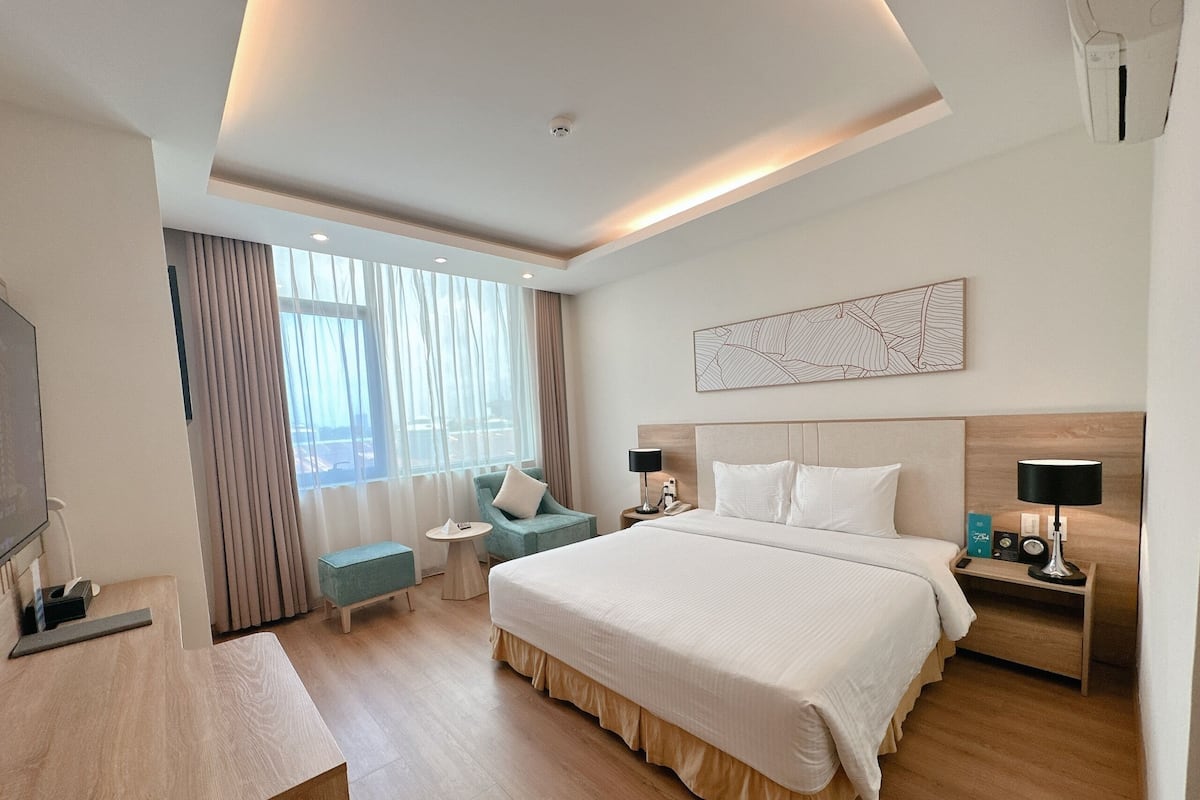 A modern hotel room with a large bed, a desk, a chair, a small table, and a TV.