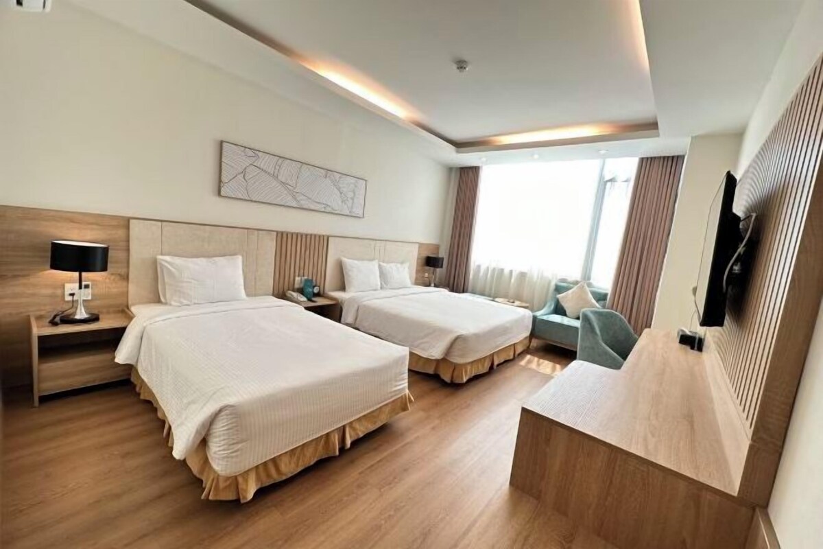 Habitación de hotel con dos camas, un escritorio, un televisor de pantalla plana y un ventanal con cortinas.