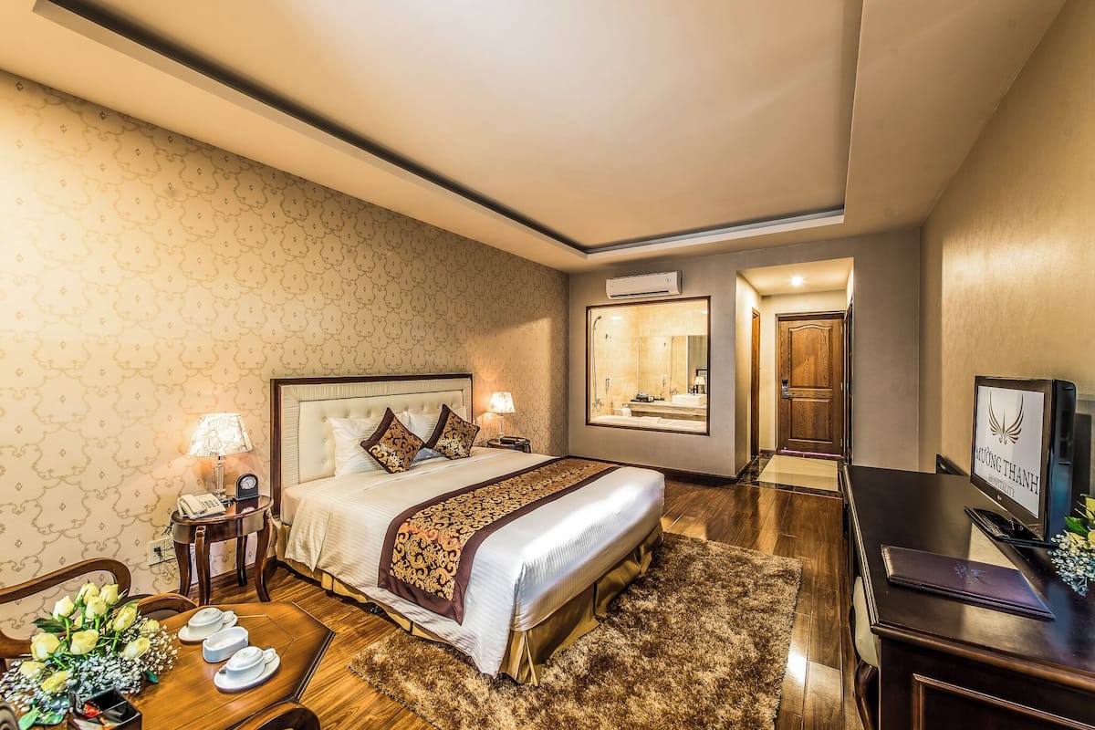 A hotel room with a large bed, bedside tables, a desk, a TV, and a mirror.