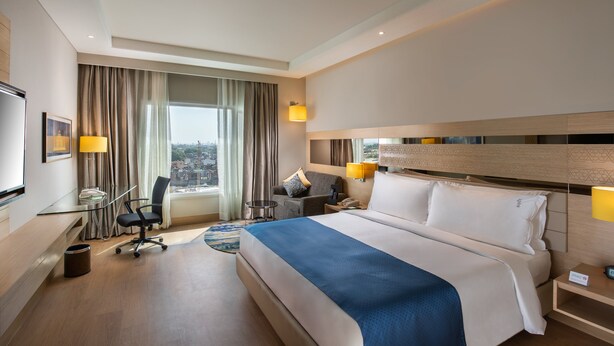 Une chambre d’hôtel moderne avec un grand lit, un bureau, une chaise et une vue sur la ville.