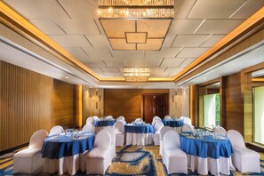 A conference room with round tables, white chairs, and blue tablecloths. - Holiday Inn Agra MG Road by IHG (Agra)
