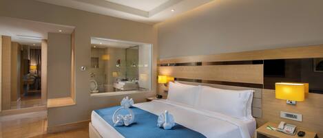 Habitación de hotel con una cama grande, una mesita de noche con lámpara, un espejo y vistas al baño.