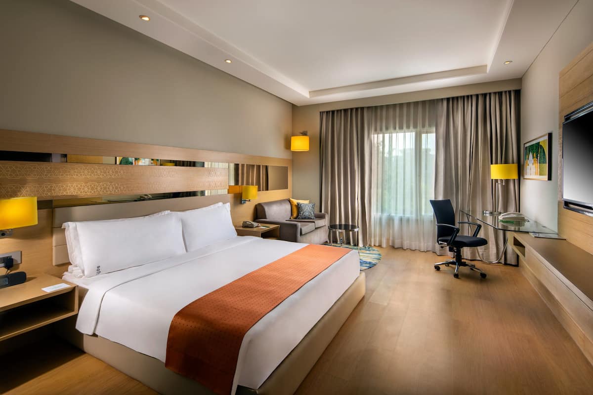 Una habitación de hotel con una cama grande, un escritorio con silla, un televisor y una ventana con cortinas.