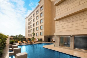 A hotel with a swimming pool, lounge chairs, and a large building with multiple windows. - Holiday Inn Agra MG Road by IHG (Agra)