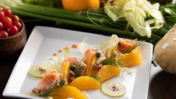 A white rectangular plate with a salad consisting of salmon, orange segments, and green herbs.