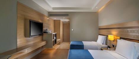 A hotel room with two beds, a television, a minibar, and a lamp.