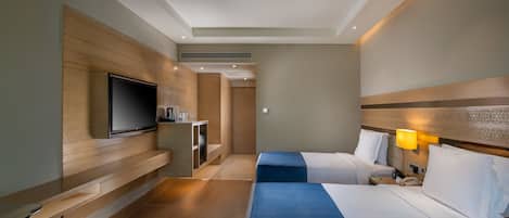 A hotel room with two beds, a TV, a desk, and a lamp.