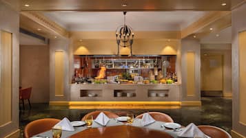 A hotel dining area with a central buffet, a chandelier, and a table set for a meal.