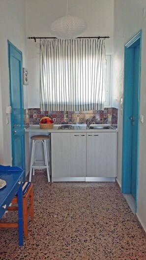 A compact kitchen with a sink, a stool, and a fruit basket on the counter.