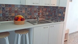 A kitchen with a tiled backsplash, a sink, and a fruit basket on the counter. - Vivian Studios (Rhodes)