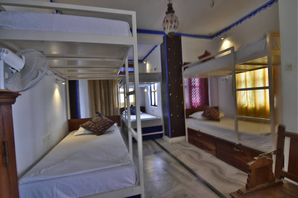 A room with bunk beds, a fan, and a window with curtains.