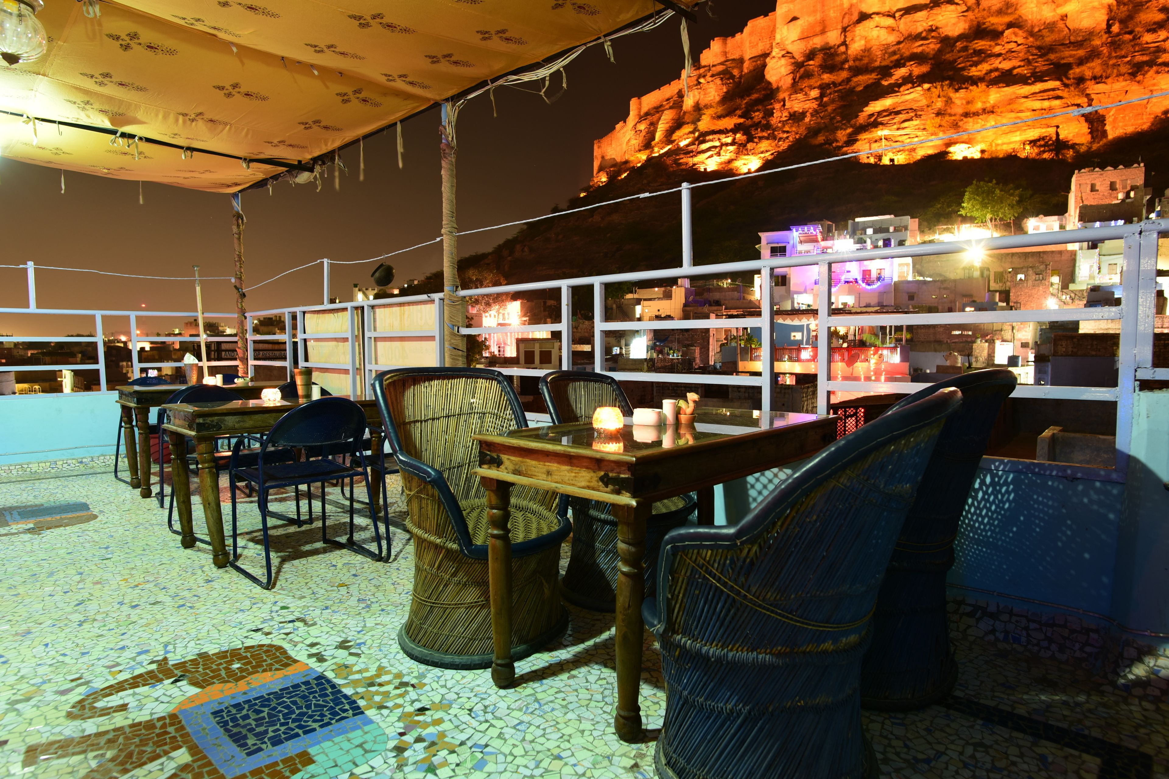 Un espacio al aire libre con mesas y sillas, piso de baldosas y vista a un acantilado rocoso por la noche.