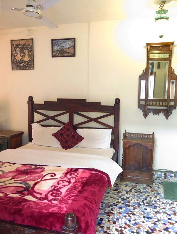 A bedroom with a wooden bed, a red and white patterned bedspread, a small wooden nightstand, a mirror, and a ceiling fan.