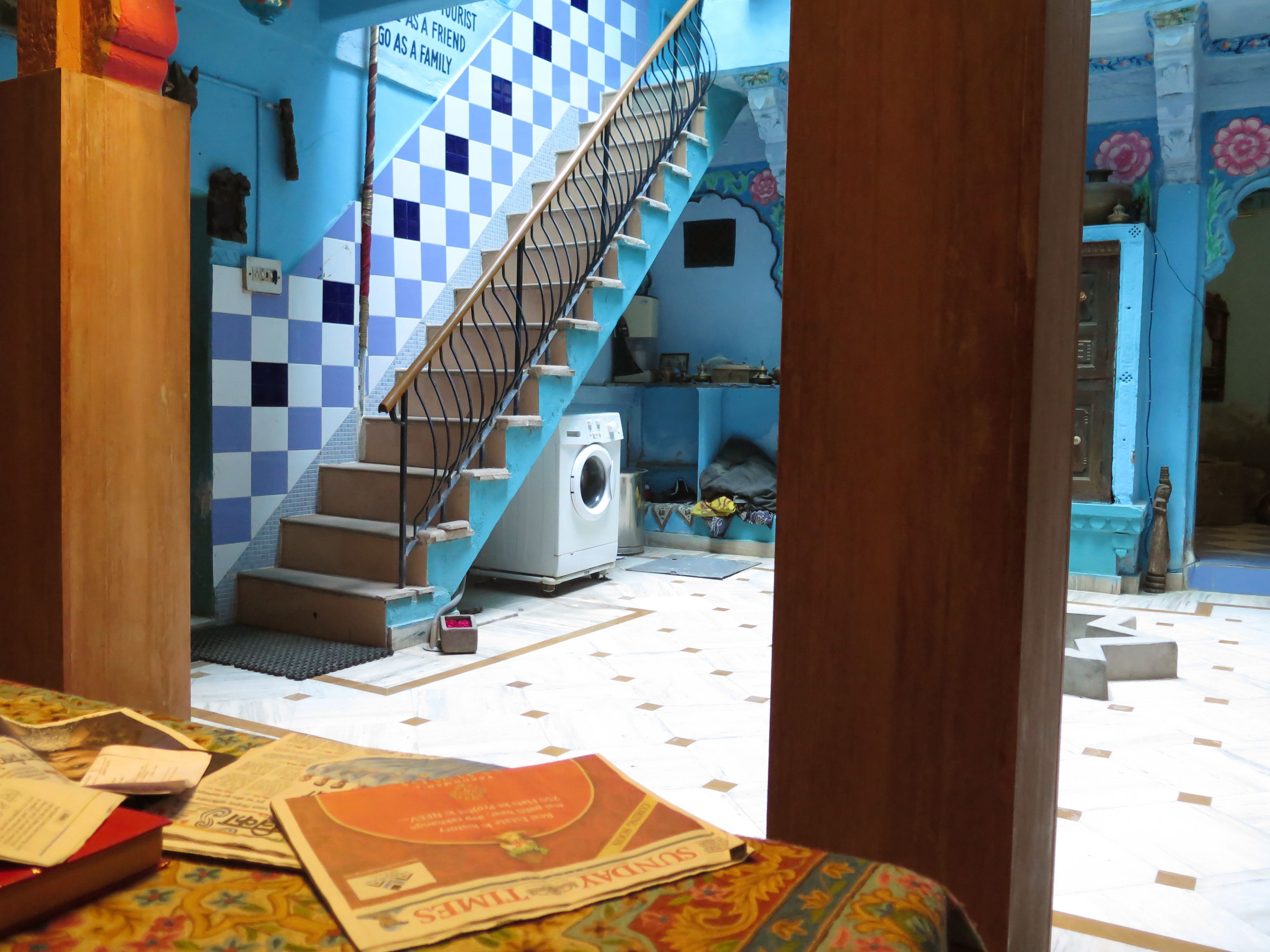 Una habitación con pared azul y blanca a cuadros, una escalera con barandilla de metal, una lavadora y una cama con colcha estampada.