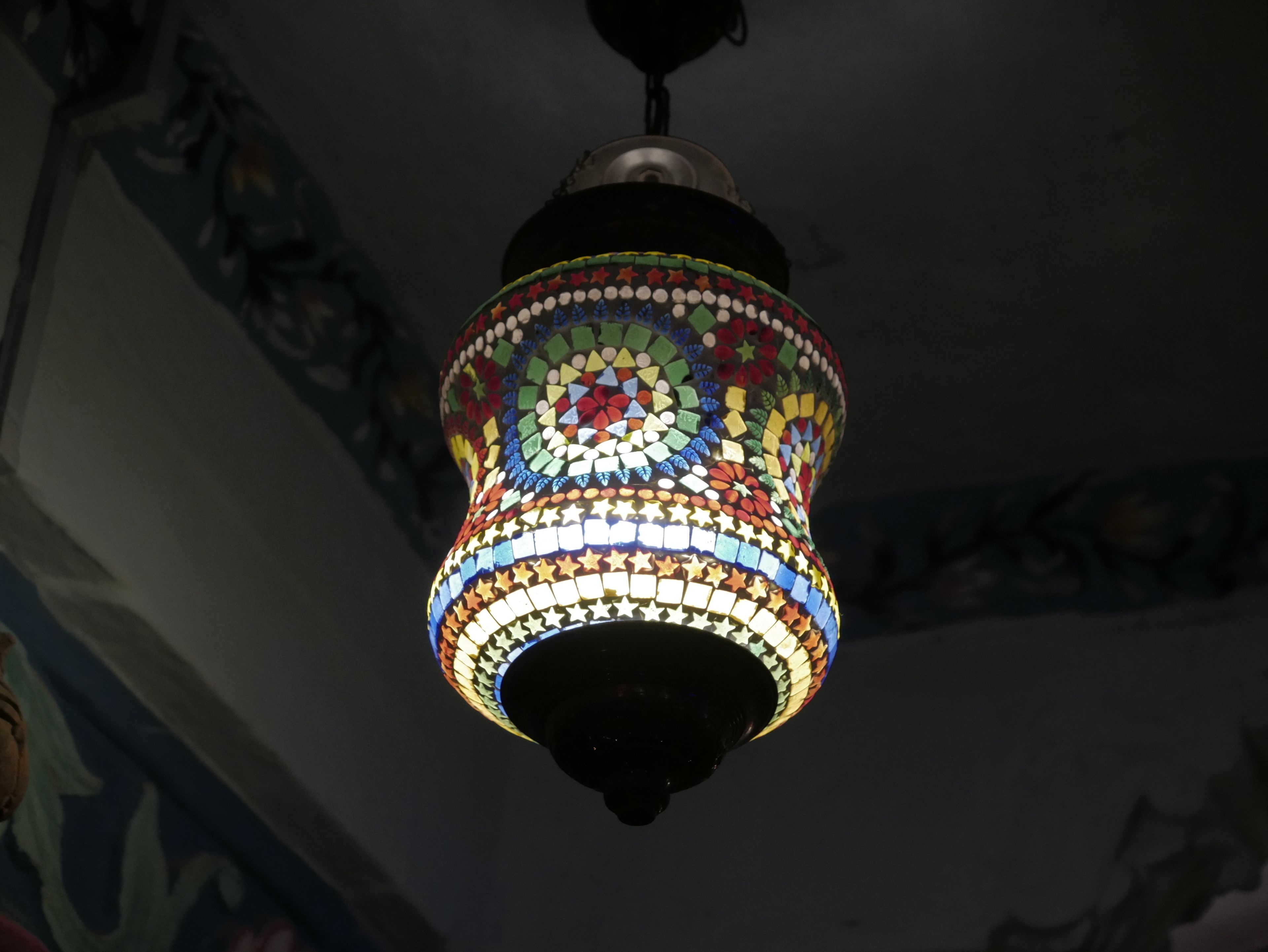 Una lámpara colgante con un diseño de mosaico, base oscura y motivos de estrellas coloridas.