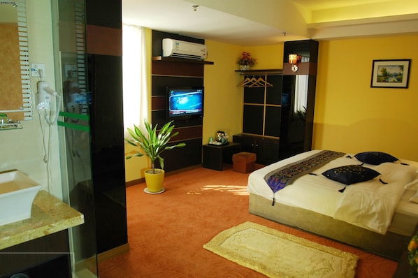 Habitación de hotel con cama, televisión, planta en maceta, mesita de noche y baño con lavabo y espejo.