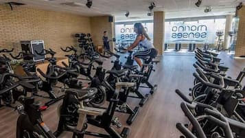 Un gimnasio con varias bicicletas estáticas dispuestas en filas, una pared de ladrillo y un ventanal grande con el texto "onone See".