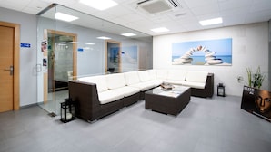 A modern waiting area with a sectional sofa, glass walls, and a beach-themed mural. - La Marina Resort (Elche)