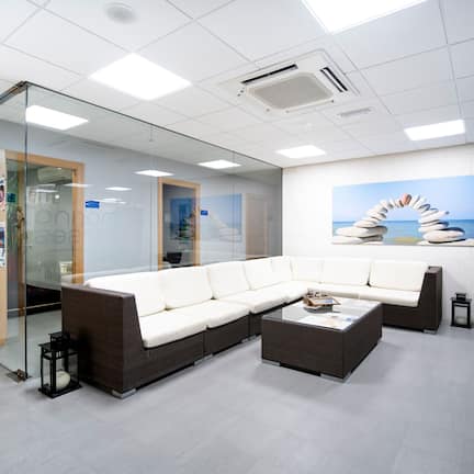 A modern waiting area with a sectional sofa, glass walls, and a beach-themed mural.
