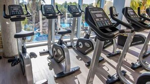 A gym with treadmills and ellipticals, large windows, and a view of palm trees and a pool. - La Marina Resort (Elche)