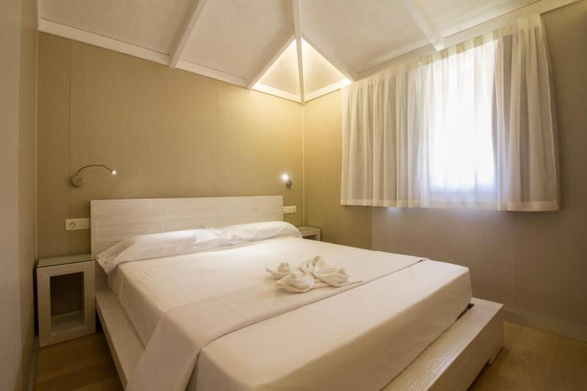 Una cama bien hecha con sábanas y toallas blancas, una mesita de noche y una lámpara de pared.