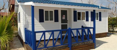 Een klein, laag gebouw met een blauw dak en witte muren, met een houten terras en een blauwe balustrade.