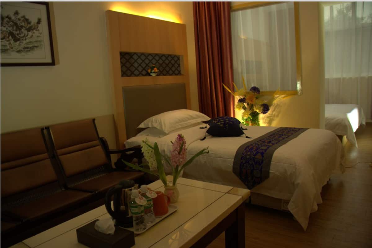 Hotelkamer met een bed, een bankje, een nachtkastje met een bloevas en een wandplank met een ingelijst beeld.