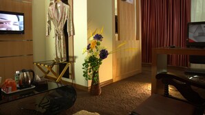Hotelkamer met televisie, badjas, vaas met bloemen, bureau met stoel en een rood gordijn.