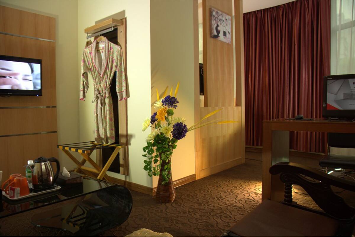 Hotelkamer met televisie, badjas, vaas met bloemen, bureau met stoel en een rood gordijn.