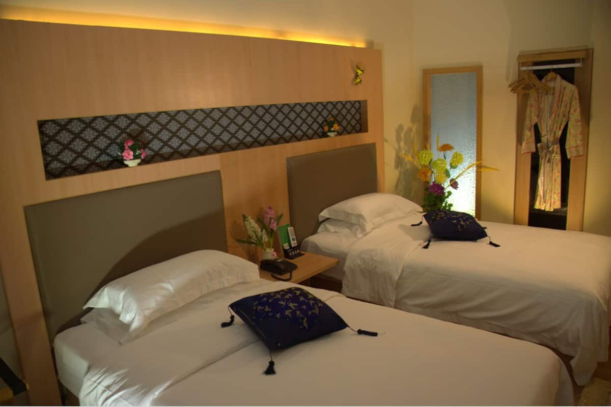 Hotelkamer met twee bedden, een nachtkastje met telefoon en een bloevas, een spiegel en een kledingrek.