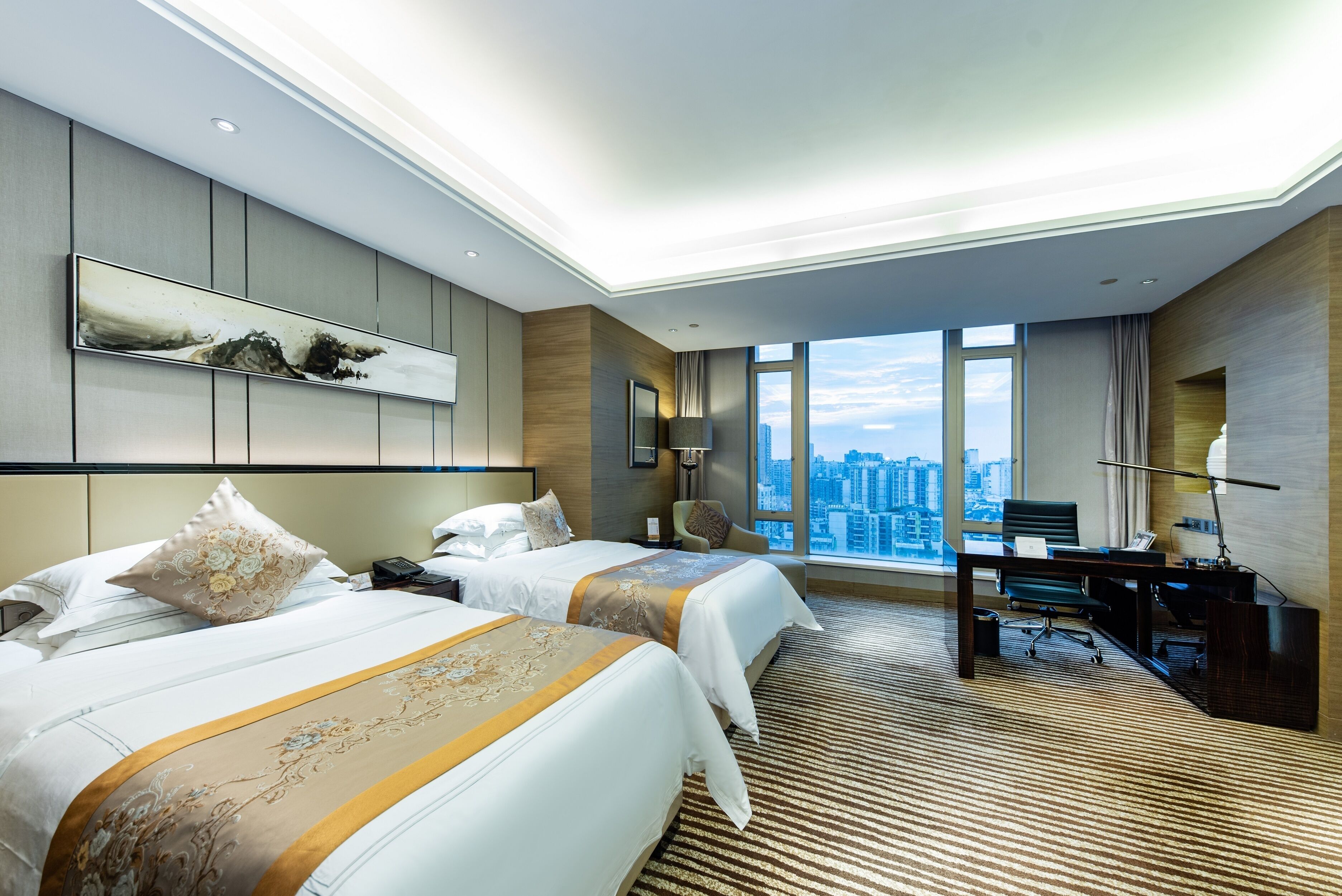 Habitación de hotel moderna con dos camas, un escritorio y un ventanal que ofrece vistas de la ciudad.